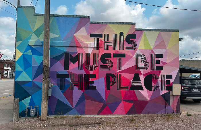 Mural A mural painted on the side of a building with a colorful geometric pattern and text reading: "This Must Be the Place"